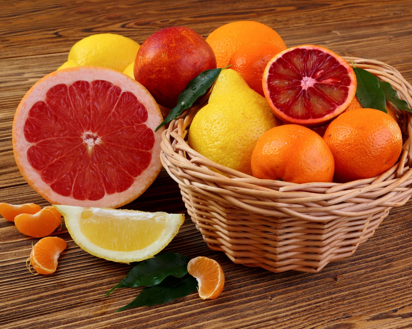 A wicker basket filled with vitamin C-rich citrus fruits like oranges, lemons, grapefruits, and tangerines on a wooden table.